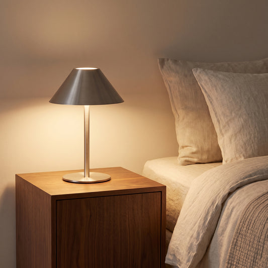 Metal bedside lamp switched on on a walnut nightstand beside a bed