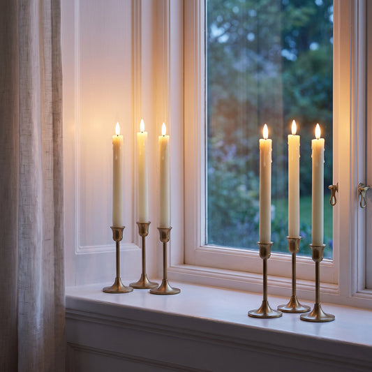 Six flameless LED taper candles glowing on a white window sill at dusk