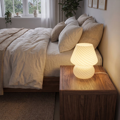 Mushroom table lamp on a walnut nightstand beside a bed at dusk
