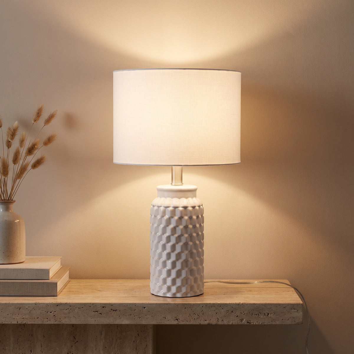 Ceramic lamp lit at night on a travertine console, warm light on the wall