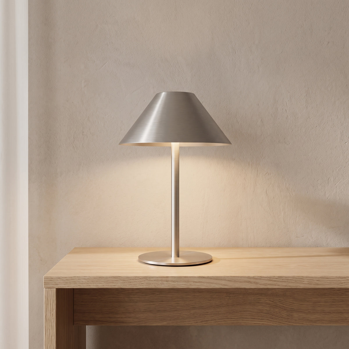 Brushed metal bedside lamp glowing softly on a light oak console