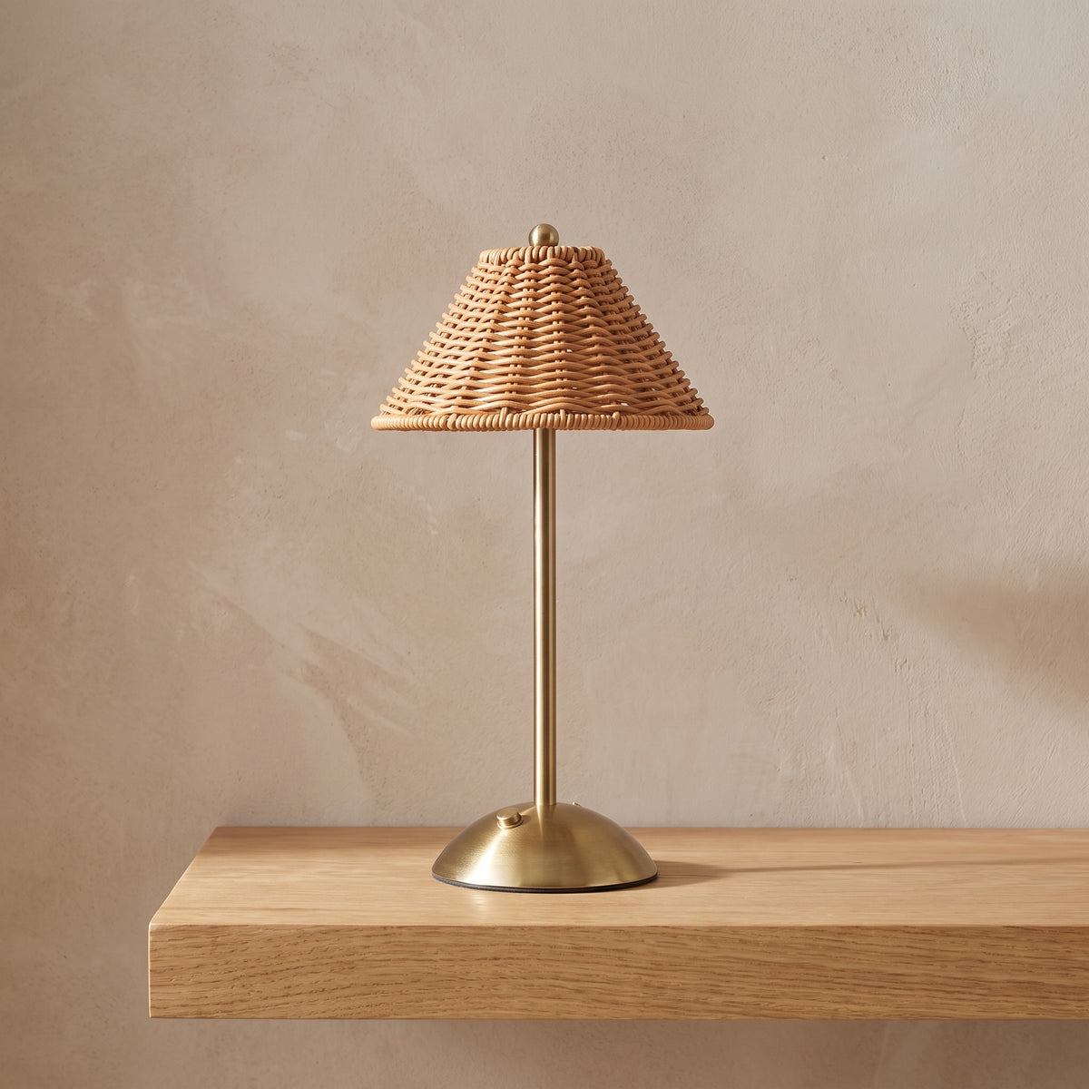 Cordless table lamp with a woven rattan-look shade on a light oak shelf
