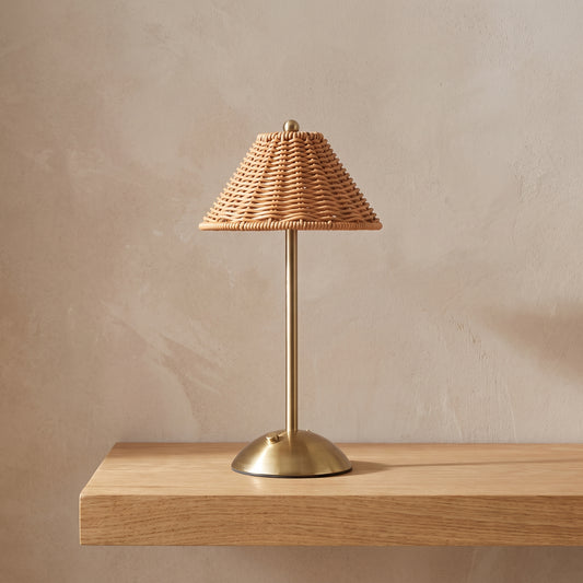 Cordless table lamp with a woven rattan-look shade on a light oak shelf