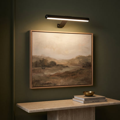Picture light casting warm light on a landscape painting above a travertine console