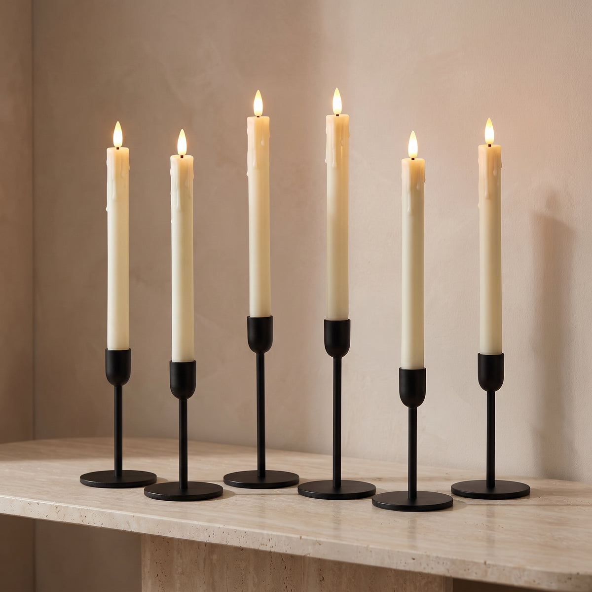 Set of six ivory flameless LED taper candles, lit, in black holders on a travertine console