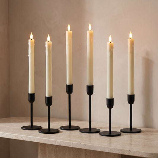 Set of six ivory flameless LED taper candles, lit, in black holders on a travertine console