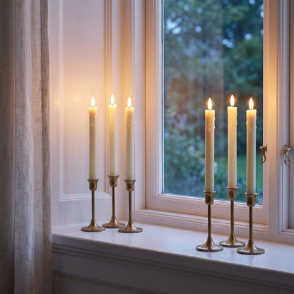 Six flameless LED taper candles glowing on a white window sill at dusk